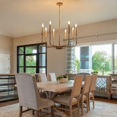 a dining room table with chairs and a chandelier hanging from the ceiling in front of large windows