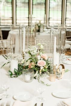 the table is set with white and pink flowers, greenery, candles and silverware