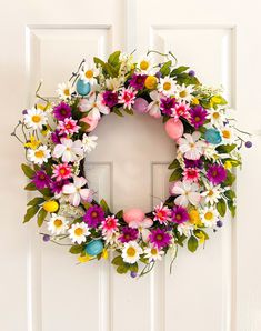 a white door with a wreath on it that has flowers and eggs painted on it