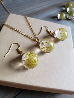 Beautifully elegant yellow flower earrings and necklace set, elegant glass orb earrings with delicate, dried flowers inside. Solid glass ball earrings have warm gold finishing and hooks. Necklace chain is 18 inches in length, and is 18k Gold plated stainless steel. In earlier centuries, a gift of flowers was a meaningful gesture meant to portray the surrounding feelings involved, and show deep affection and appreciation for the receiver. It was known, yellow was worn as a representation of luxur Minimalist Glass Jewelry With Ear Wire, Dainty Yellow Flower Shaped Jewelry, Adjustable Flower Glass Jewelry, Adjustable Glass Flower Jewelry, Flower Pendant Jewelry With Ear Wire For Gift, Adjustable Flower-shaped Glass Jewelry, Gold Drop Earrings With Pressed Flowers, Adjustable Resin Jewelry With Pressed Flowers, Gold Round Resin Flower Earrings