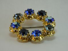 Austrian Crystal Blue Brooch Vintage Signed made in Austria, gold tone open design circular pin Each brilliant blue crystal is pronged set  Three color variations of brilliant blue stones The clarity & brilliance of the glass is known as lead crystal Absolutely beautiful In excellent vintage condition Secured pin has lost some finish Diameter 1 3/4 inches The vintage jewelry we sell has been cleaned.  Happy to answer any questions.  Please see my other listings. Blue Round Brooch For Formal Occasions, Formal Blue Round Brooch, Formal Blue Round Brooches, Blue Crystals Stones, Blue Brooch, Blue Stones, Crystal Blue, Brooch Vintage, Crystal Stones