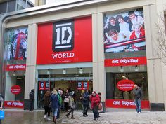 people walking in front of a store with red and white advertisements on the building's windows