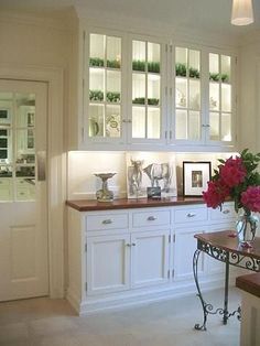 a kitchen with white cabinets and pink flowers in vases on the counter top next to a bench