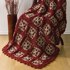 a red crocheted blanket sitting on top of a chair next to a potted plant