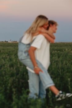 two people standing in the middle of a field with their arms around each other as they hug