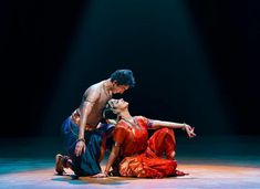 a man and woman performing on stage with lights in the background, one holding the other's leg