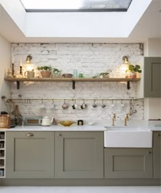 a kitchen with white brick walls and green cabinets, potted plants on the shelves