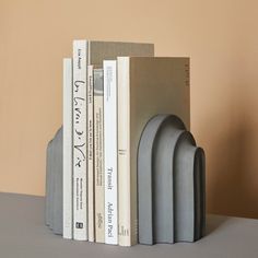 three books are stacked on top of each other in front of a beige wall and two gray bookends