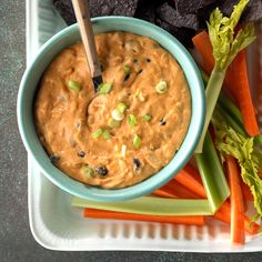 a blue bowl filled with dip surrounded by carrots and celery next to tortilla chips