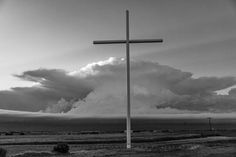 black and white photograph of a cross in the middle of an open field with clouds