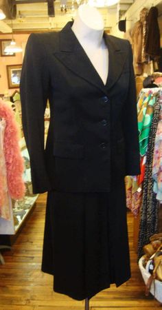 This is a black wool gabardine suit from the early 1940's.  It features a fitted jacket with medium wide notched lapels and a wide shoulder line, and a skirt with 3 inverted pleats in the front and the back. The skirt opens with a well working metal zipper.  The label is from Schmitt's Clothier's in Milwaukee.  The jacket is lined in black sateen.  There is hand done topstitching around the lapels.  I didn't find any problems or issues. It's in great condition!   Comes from a smoke free home.Mea Classic Formal Skirt Suit With Notch Lapel, Classic Evening Skirt Suit With Notch Lapel, Classic Black Skirt Suit For Work, Tailored Classic Career Skirt Suit, Classic Tailored Skirt Suit For Semi-formal Occasions, Classic Black Skirt Suit For Semi-formal Occasions, Black Skirt Suit With Suit Collar For Formal Occasions, Classic Notch Lapel Skirt Suit For Career, Classic Tailored Skirt Suit With Suit Collar