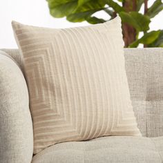 a close up of a pillow on a couch with a plant in the back ground