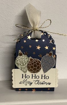 a christmas card hanging from the side of a shelf with gold stars and an ornament on it