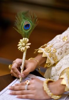 a woman is holding a peacock feather on top of a piece of paper and writing