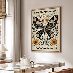 a butterfly painting hanging on the wall above a table with a cup and saucer