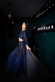 a woman in a blue dress standing next to a shelf with bottles on the wall