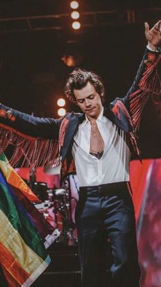 a man in a suit and tie on stage with his arms outstretched, holding a flag