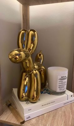 a gold balloon dog sitting on top of a stack of books next to a cup