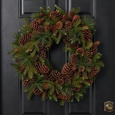 a wreath with pine cones and evergreen needles hangs on the front door to welcome guests