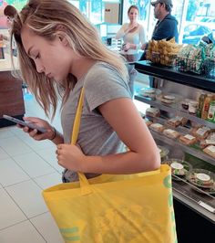 a woman is looking at her cell phone while holding a yellow bag in front of her