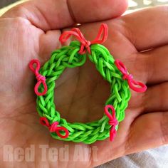 a hand holding a small green and pink ring with red bows on it's end