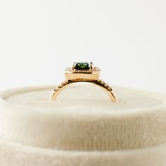 a gold ring with a green stone in it on top of a white box,