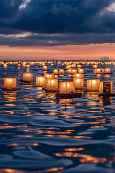 many lanterns floating in the water at night with lights on them and dark clouds above