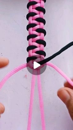 two hands holding a pink and black piece of string