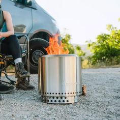 a woman sitting in front of a campfire next to a bike