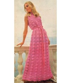 a woman in a pink crocheted dress standing on a balcony