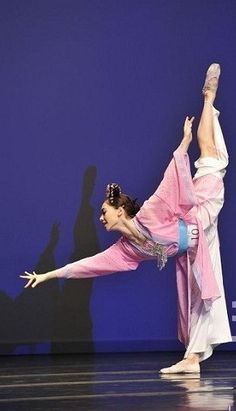 a woman in a pink and white outfit doing a dance move on stage with her legs spread out