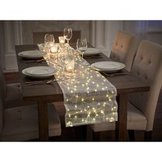 a long table with white plates and glasses on it is lit up by yellow lights