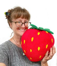 a woman is holding a large stuffed strawberry