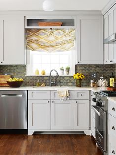 a kitchen with white cabinets and wood floors is pictured in this image, there are yellow flowers on the window sill above the dishwasher