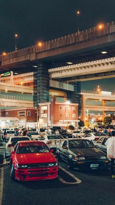 many cars are parked in a parking lot near an overpass at night with lights on