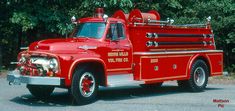 an old red fire truck parked in front of some trees