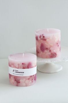 two candles sitting next to each other on a white table with pink flowers in them