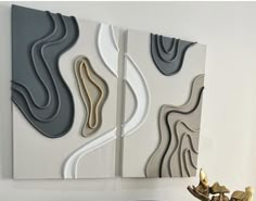 two abstract paintings on the wall next to a vase with gold and silver flowers in it