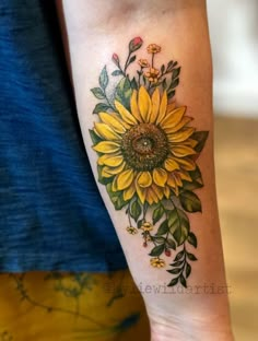 a woman's arm with a sunflower and leaves tattoo on the left forearm