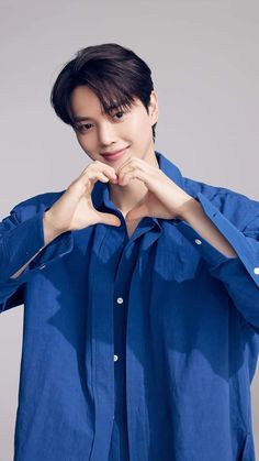 a young man is posing with his hands in the shape of a heart while wearing a blue shirt