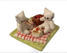 two white cats sitting on top of a green plate with food in front of them