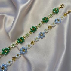 a close up of a necklace on a white satin surface with gold and green beads