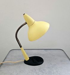 a yellow desk lamp sitting on top of a gray table next to a white wall