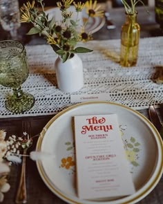 a table setting with place settings and flowers in vases on the side, along with menu cards