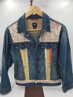 Introducing our one-of-a-kind upcycled denim jacket, handcrafted with a touch of bold and unique style that is sure to make you stand out in a crowd. Made from recycled denim, this jacket has been given a new lease of life and features a vibrant floral design in shades of blue, pink, green and white, accentuated with an eclectic mix of shapes and patterns. To truly stand out, we've added a matching purse to the set, crafted from a matching pillow sham, that'll be an absolute head-turner. The purse is specially designed to complement the jacket, with the same vibrant floral patterns and colors on display. Both the jacket and purse have been carefully made and feature superior craftsmanship, considering every small detail to ensure that it's not only stylish, but also functional. With its on Spring Upcycled Recycled Denim Jacket, Reworked Recycled Denim Jacket For Spring, Spring Reworked Recycled Denim Jacket, Casual Reworked Denim Jacket, Reworked Recycled Denim Outerwear For Spring, Spring Cotton Reworked Denim Jacket, Spring Reworked Outerwear In Recycled Denim, Spring Reworked Cotton Denim Jacket, Spring Reworked Denim Jacket