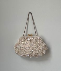 This is a beautiful vintage 1960s beaded white flower purse! It is a snap purse with one compartment inside, white satin lining, and gold hardware. This bag is covered in lovely white beads that shimmer and turn a slight pink shade in the light. It was hand made in Hong Kong in the 60s. It is turly a unique and timeless piece! Tag: Hand Made in Hong Kong Materials: White beads, gold hardware and satin lining. Measurements: Length: 8.5" Width: 1" Strap: 6" Condition: Great! All beads in place, just a few light marks on the inside lining and slight fading on gold strap (as pictured). Vintage 1960s white beaded floral purse, Vintage hand made in Hong Kong beaded wrist strap purse, 1960s beaded formal evening pursed Flower Beadwork, Formal Purse, Snap Purse, Bag For Wedding, Fancy Purses, Fancy Event, Sequin Flower, Flower Purses, Floral Purse