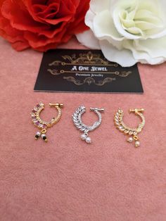 three pairs of earrings sitting on top of a pink blanket next to a white flower