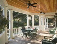 a covered porch with tables and chairs under a ceiling fan that is hanging from the ceiling