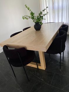 a wooden table with black chairs and a plant in the vase on it's end