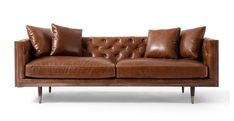 a brown leather couch sitting on top of a white floor next to two wooden legs